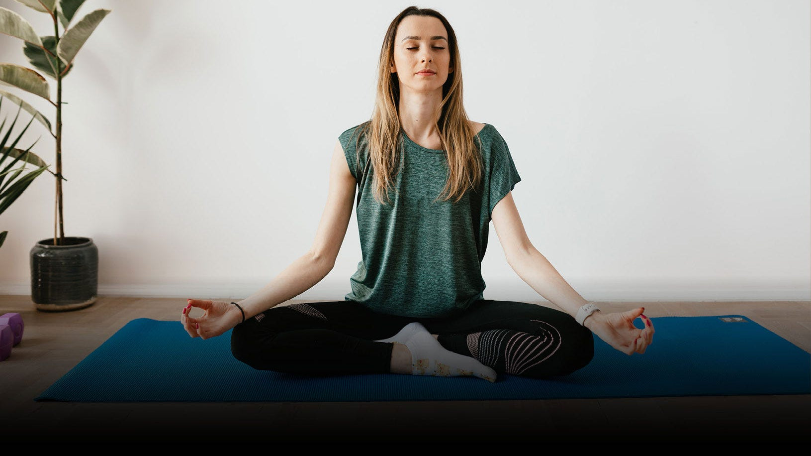 a lady sitting on the floor on a blue mat in a Yoga pose