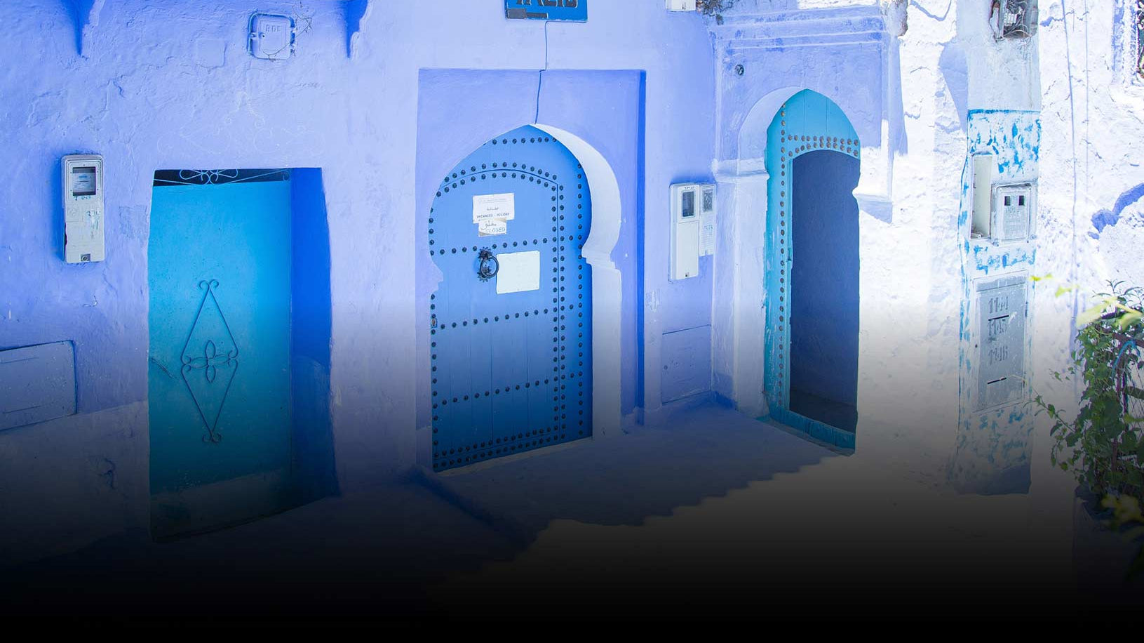 A street scene in Chefchaouen, Morocco, featuring iconic blue walls and doors with arched frames. Soft sunlight creates a serene, tranquil atmosphere.