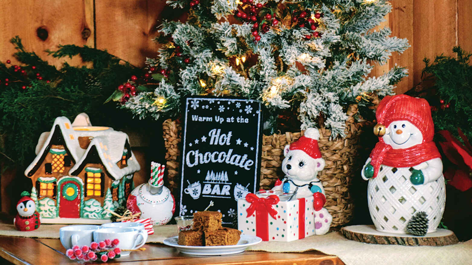 A variety of Christmas themed candle holders in front of a frosted Christmas bush.