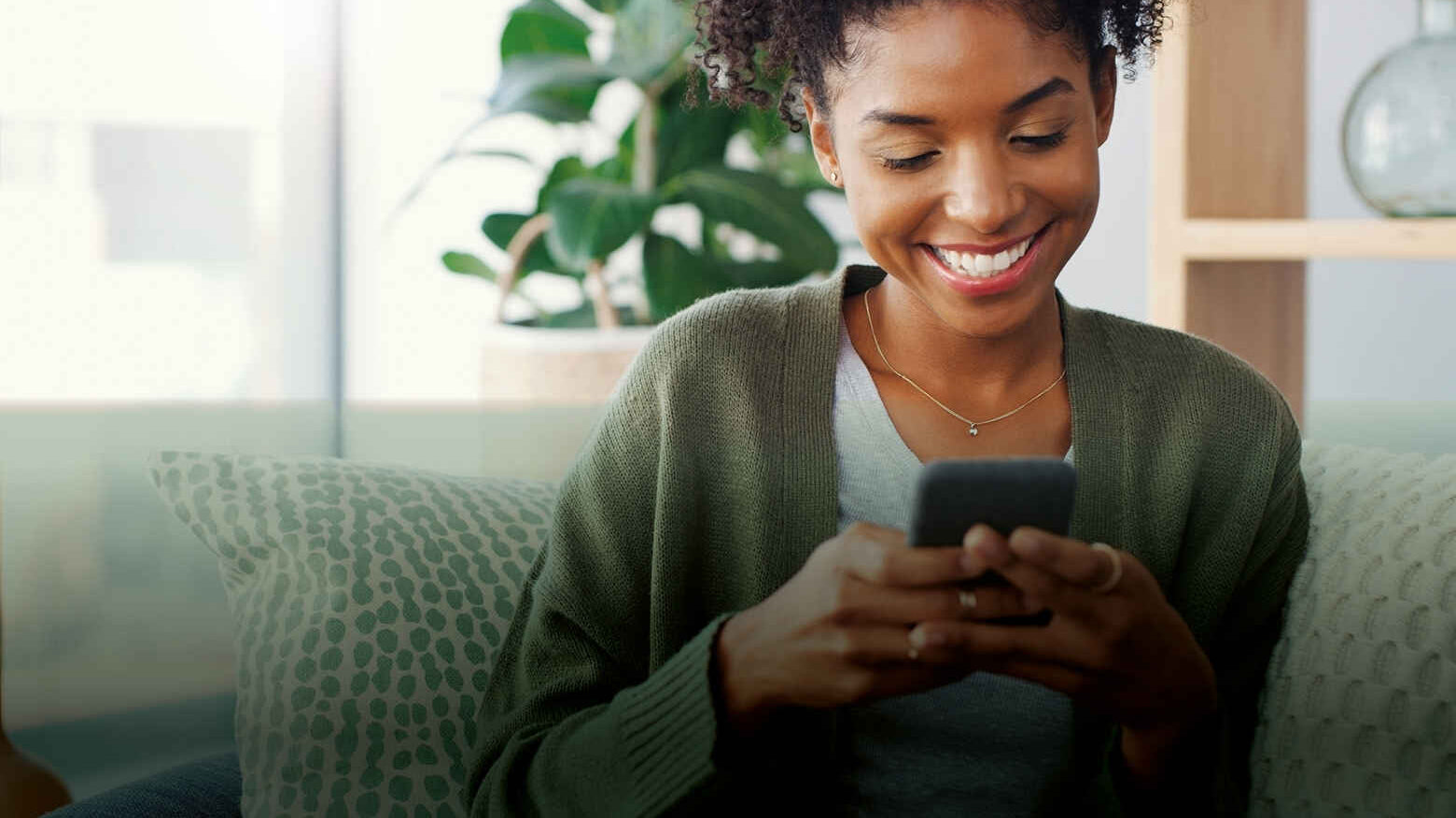 A lady smiling holding her phone in a living room setting.