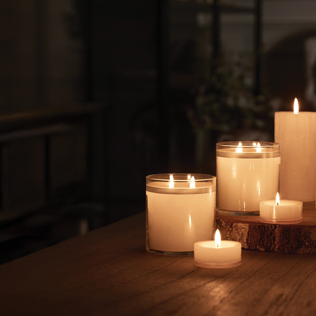 GloLite Pillars, Jar Candles, and Large Tealights on a table in a darkened room.
