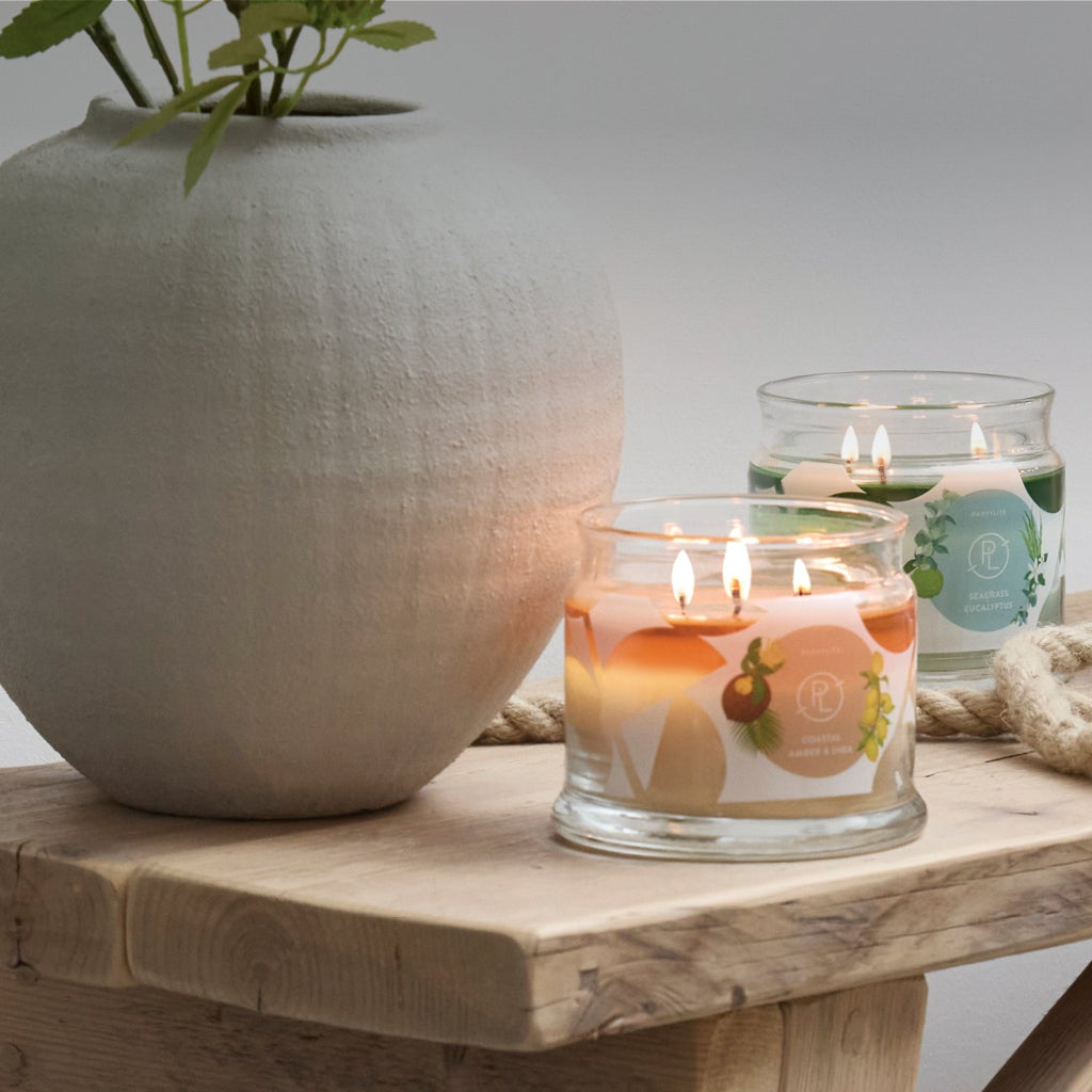 Three 3-wick jar candles with nautical decorations on a wooden table.