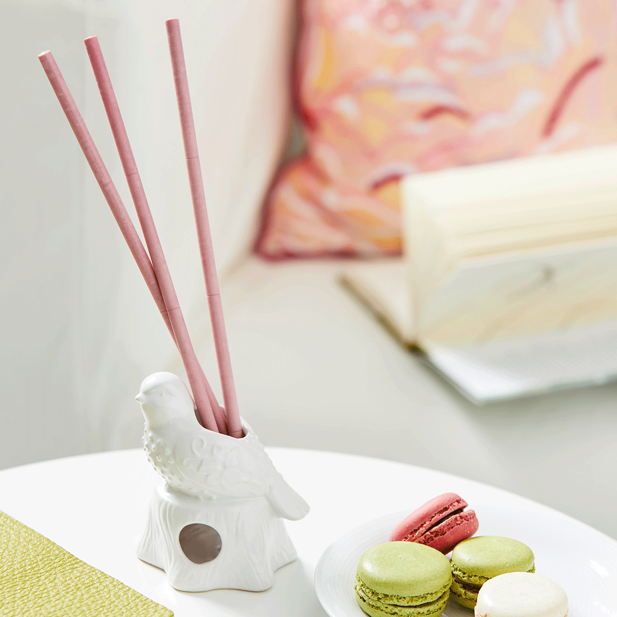Decorative bird Smart Scents stick holder with pink sticks on a white surface with macarons.