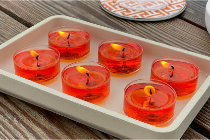 Red candles in glass holders on a white tray with a wooden surface background
