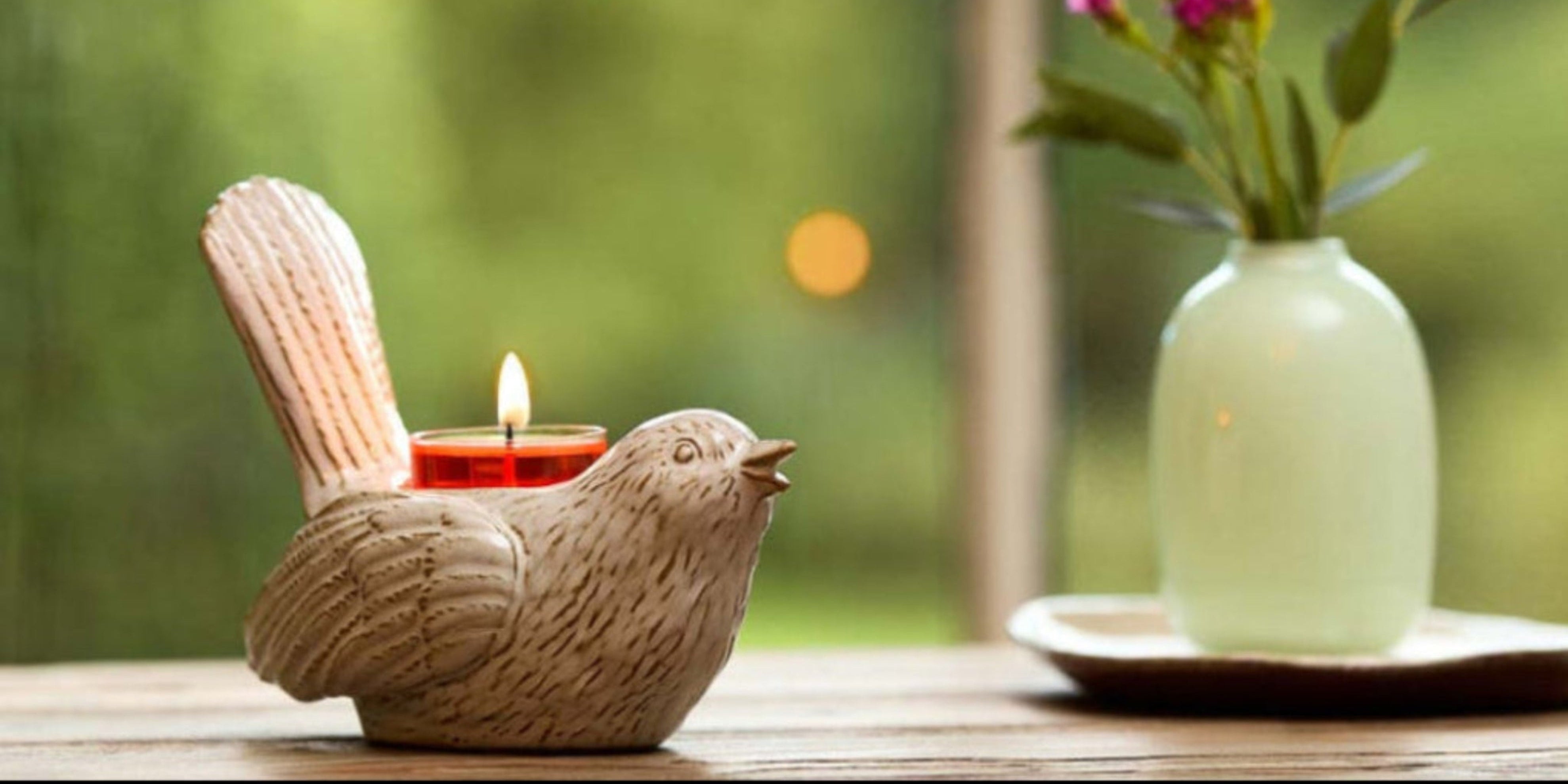 Songbird tealight holder on a wooden table next to vase of flowers on tray