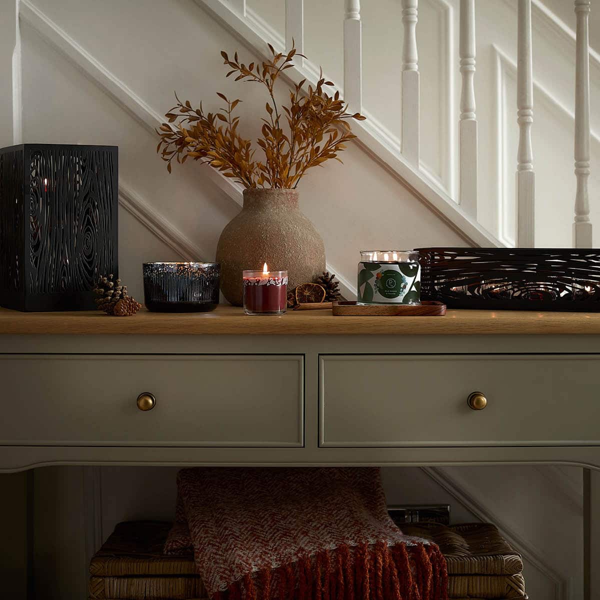 Autumn Sangria Mini Jar Candle lit, with an 3-wick Jar Candle and a Ripple Jar Candle next to a vase of flowers on a hallway table.
