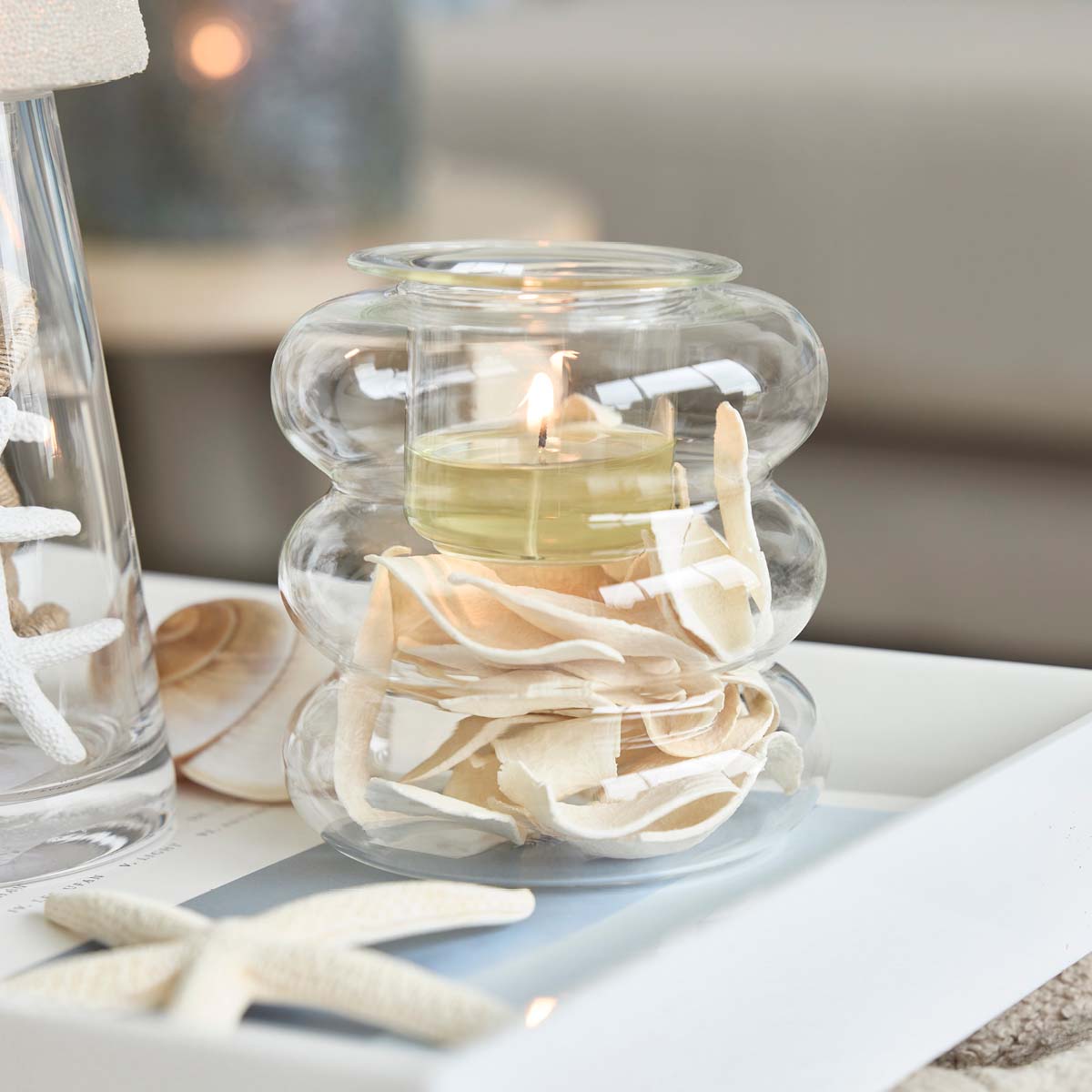 Illusion Tealight Holder with a lit candle and decorative wood chippings with a star shaped item on a white table top.