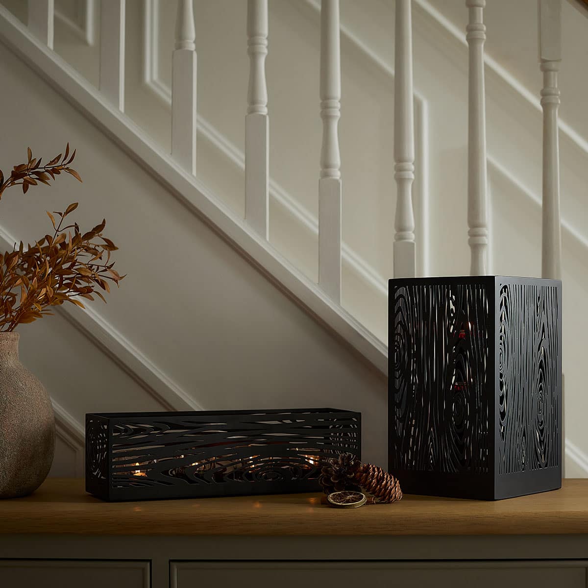 Wood Grain Hurricane shown with matching tealight holder with lit candle inside, on a hallway cabinet with white stair bannisters in the background.