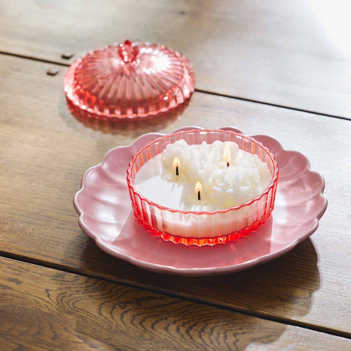 Garden Beauty Specialty Jar - In Full Bloom lit on a pink plate with the jar lid next to it on a wooden surface.