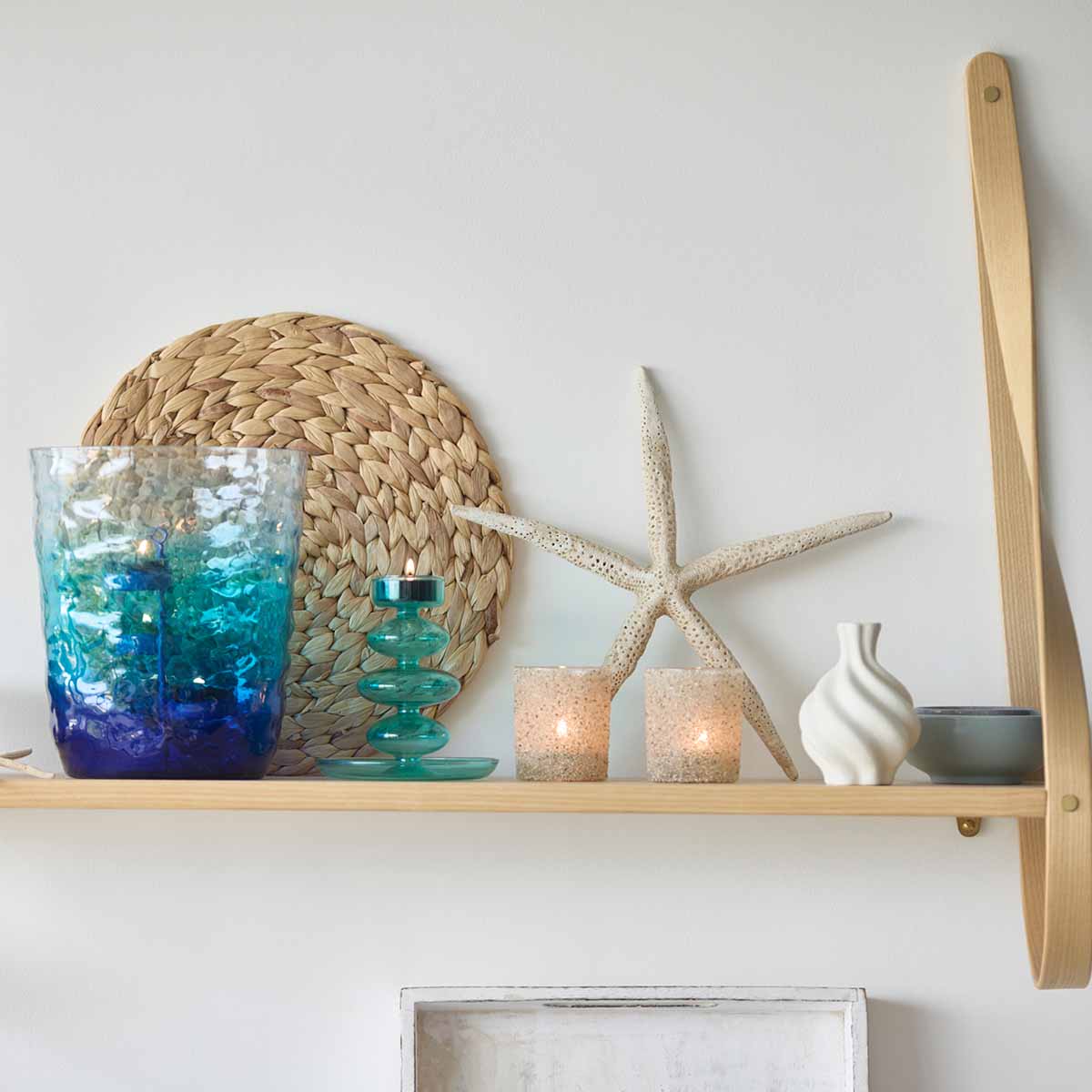 Sand Dune Tealight/Votive Holder with a star shaped decorative item behind it and a Blue/green hurricane and green tealight holder next to it against a white wall.