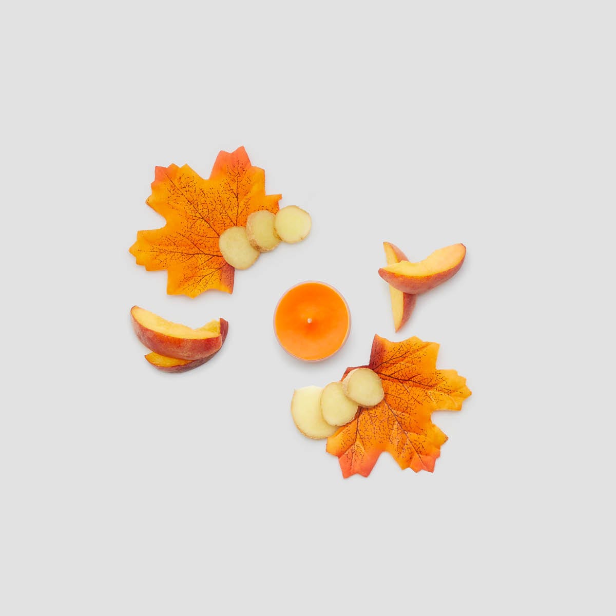 Single Maple Leaf & Ginger orange tealight with pieces of sliced fruit and maple leaves against a white background.