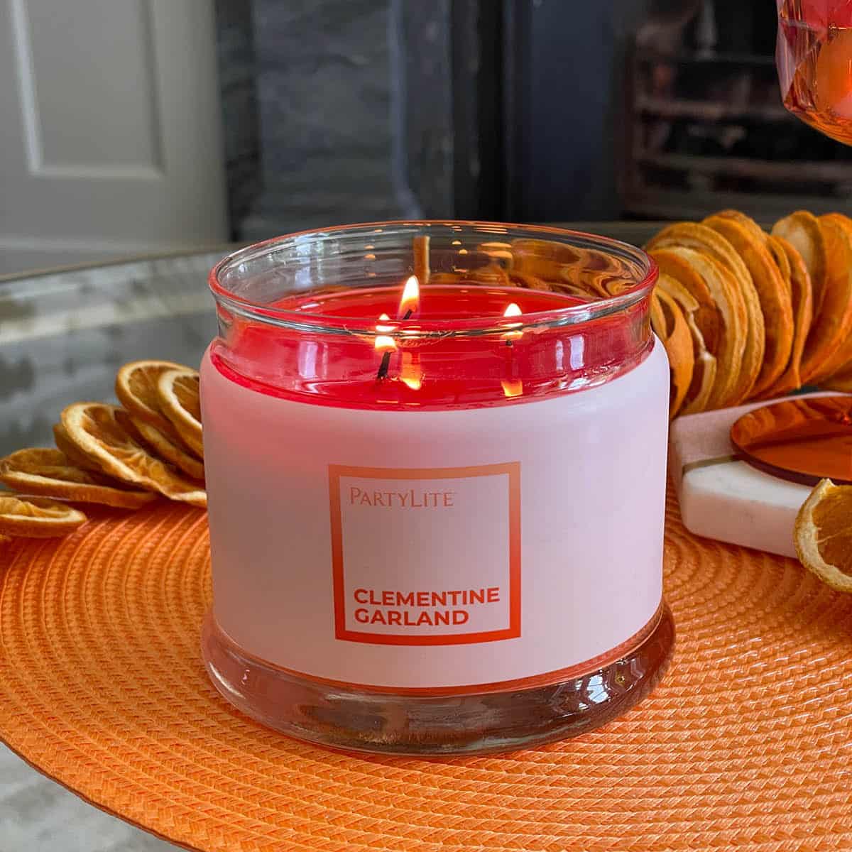Clementine Garland 3-wick jar candle lit on a texured mat.