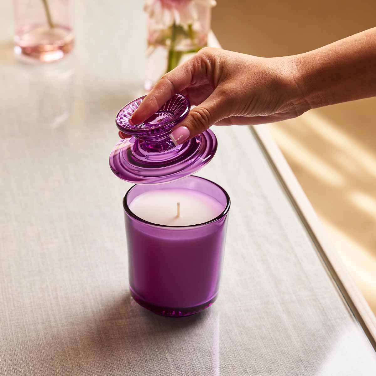Wildflower Walk Specialty Jar Candle on a light wooden surface with a hand lifting the lid from the Jar.