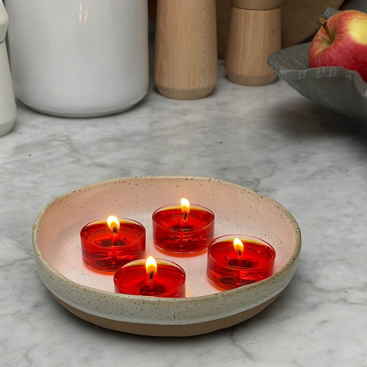 Four lit tealights in a ceramic bowl on a kitchen work surface.