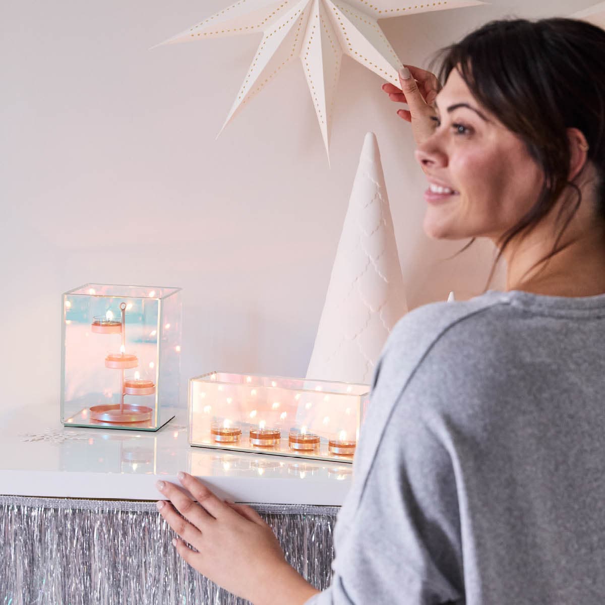 Infinite Reflections Centerpiece, shown with the hurricane, both with lit tealights and a lady placing a white star on the wall above them.