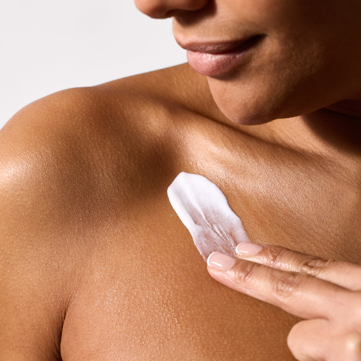 close up of a woman's shoulder with her hand applying body lotion.
