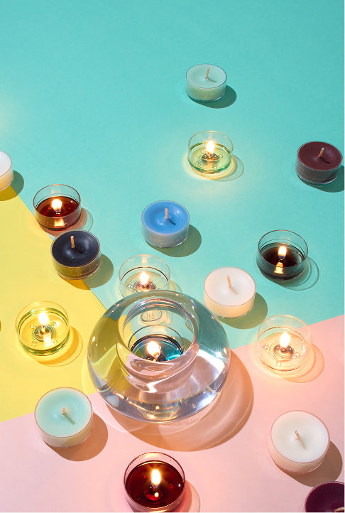 Lit and unlit variety of tealight candles surrounding a round glass holder on a geometric styled background