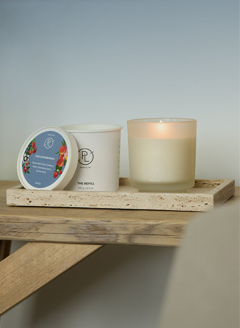 Candle jar and refill on a wooden tray upon a wooden shelf with a neutral background