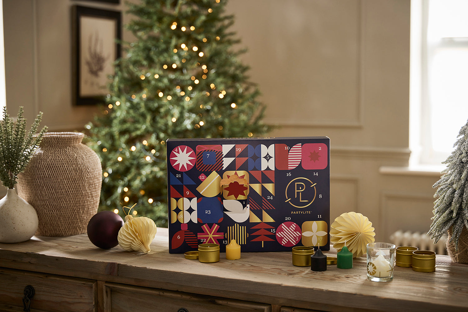 Advent Calendar with an assortment of colorful votives with a votive holder and Christmas decorations on a wooden cabinet.