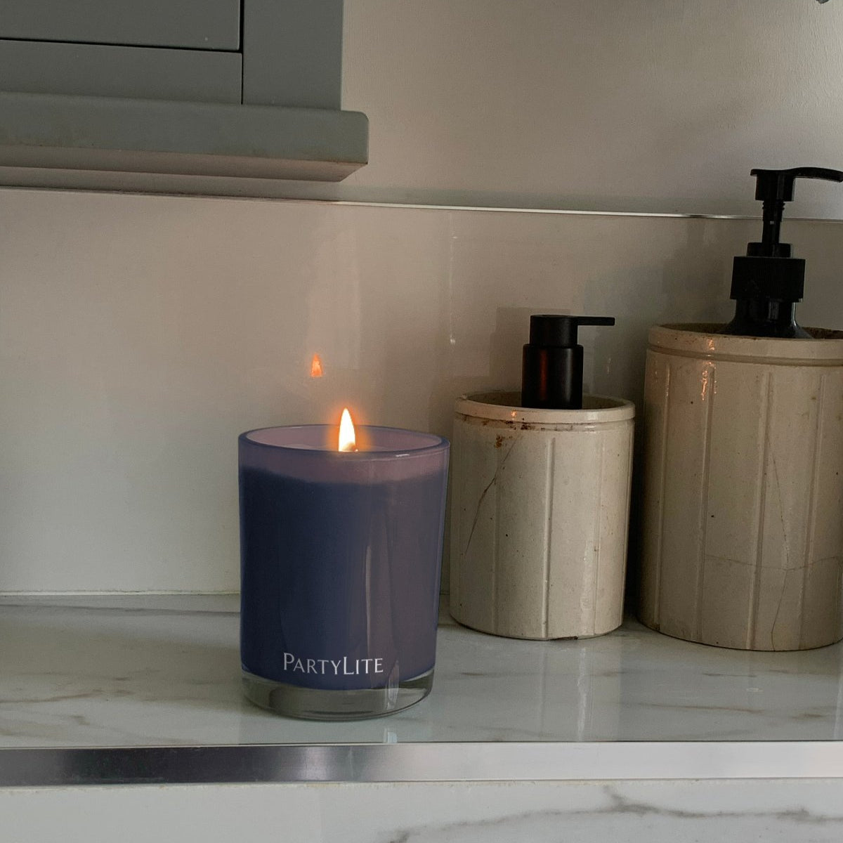 Winter Nights escential jar candle shown lit on a bathroom surface with hand wash lotions in the background.