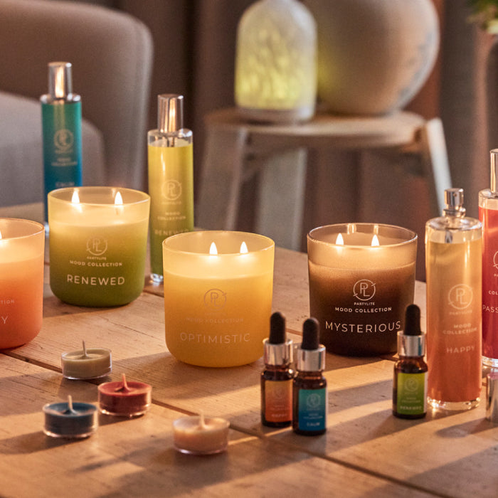 Candle jars, sprays, oils and tealights from the Mood collection displayed on a wooden table with a blurred background