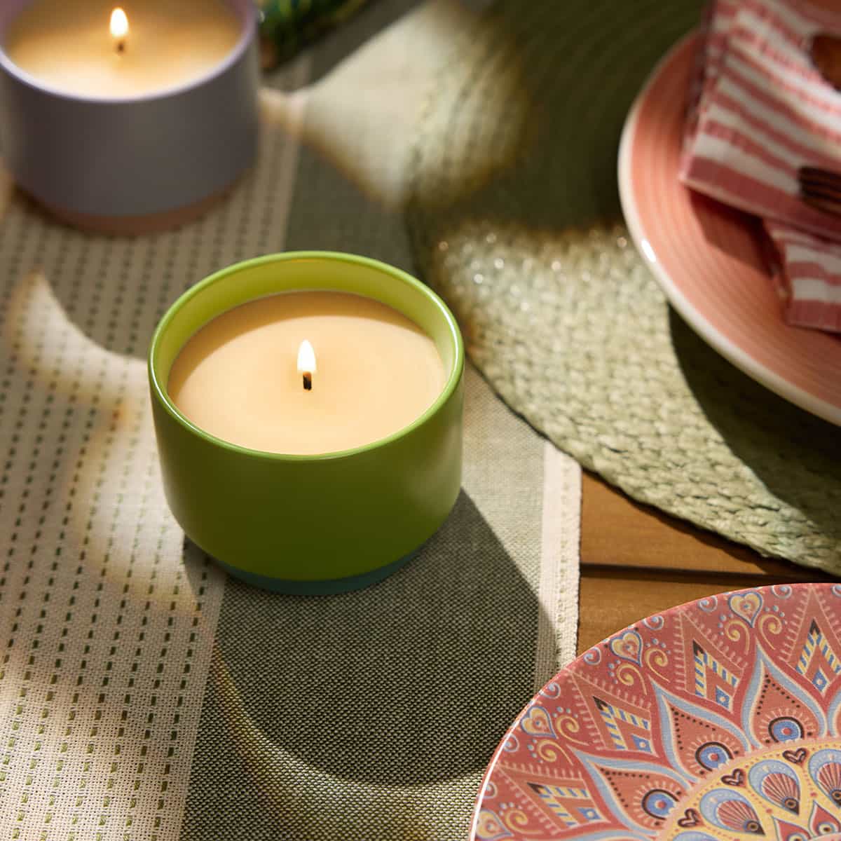 Two single wicks Citronella Jar Candles on a green and cream table runner on a wooden table with decorative plates