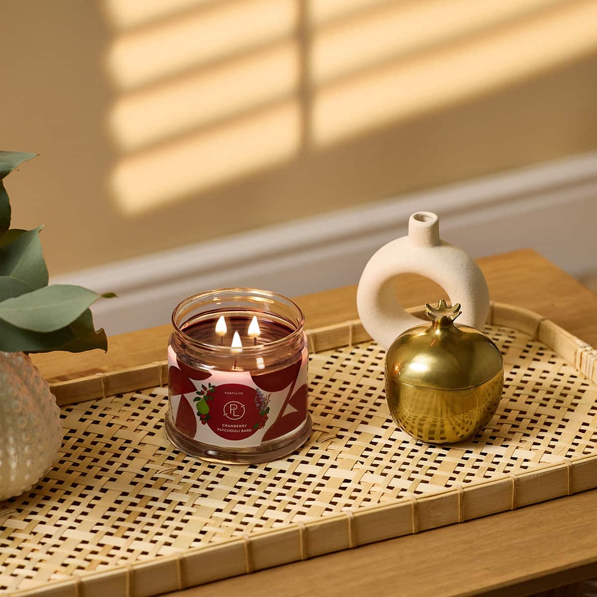 Cranberry Patchouli Bark 3-Wick Jar Candle with a Gold item and a empty white vase next to the Jar on a textured wooden tray on a wooden surface with a beige background