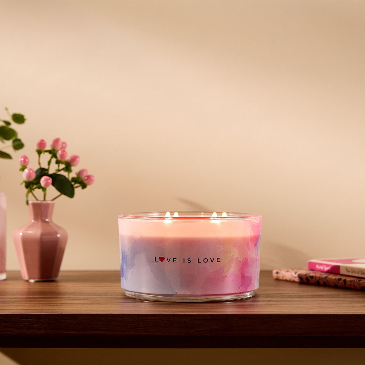 Love is Love 4-wick Jar Candle shown on a wooden table top with a vase of flowers next to it, against a beige background