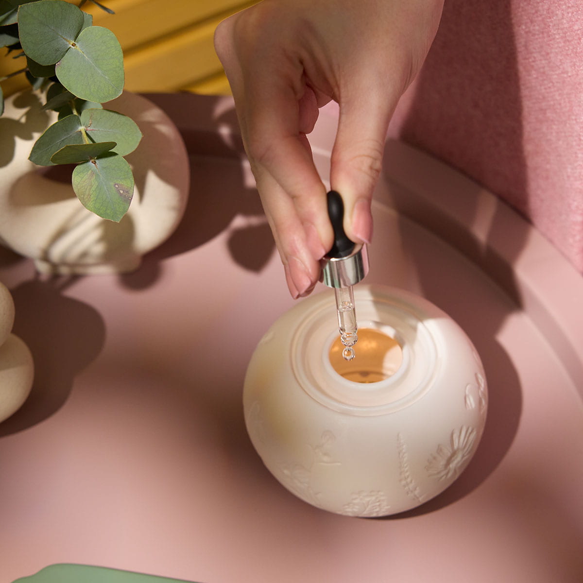 Illuminescents Blooming Fields Fragrance Warmer shown with a persons hand adding oil to the Fragrance warmer on a table
