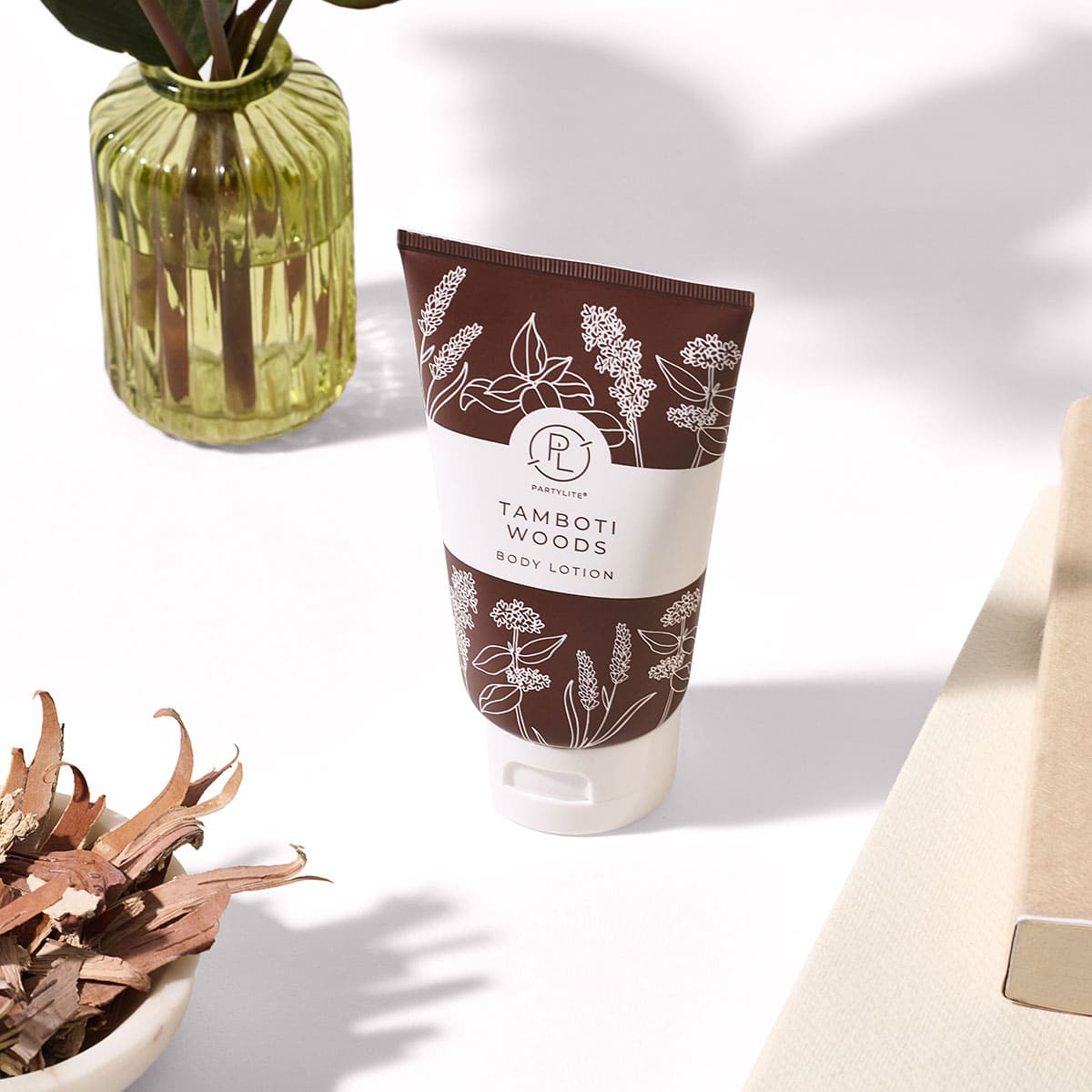 Tamboti Woods Body Lotion shown on a white surface with a clear green glass vase in the background