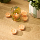 Grapefruit Peach Paloma Tealights shown with a Tealight Holder on a wooden surface with a plant pot in the background