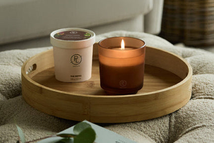 Refillable candle jar and refill candle on a wooden tray with a blurred background of a living room