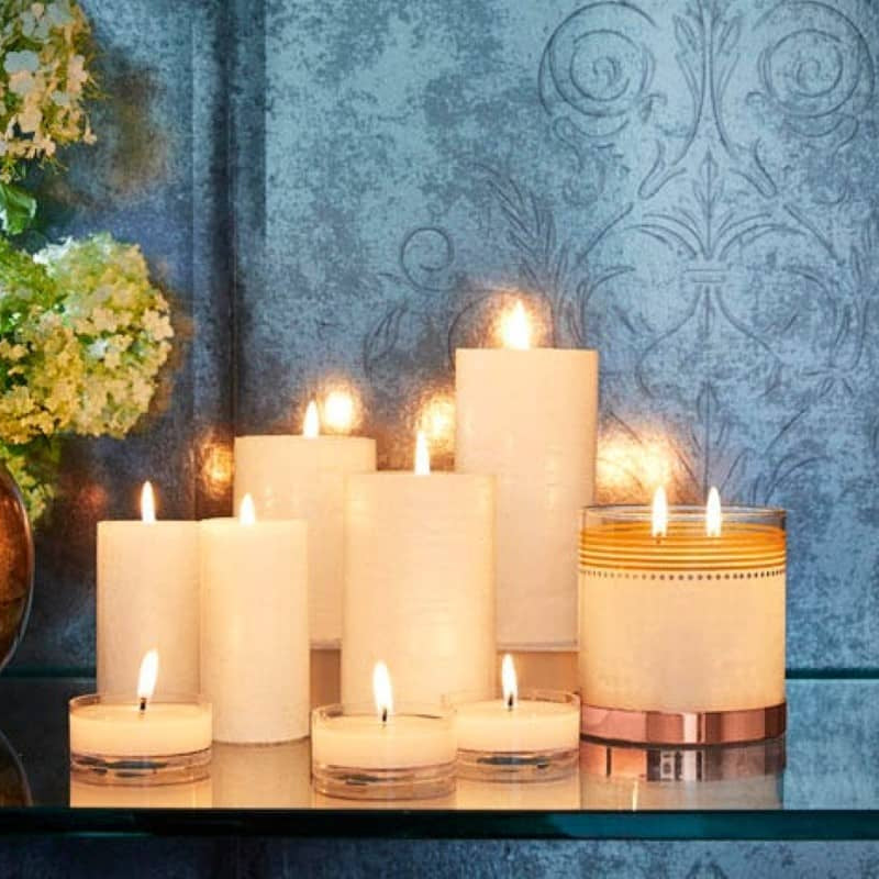 GloLite Collection, Pillar candles, Jar candles and Large tealights on a mirrored surface against a bluey grey background.