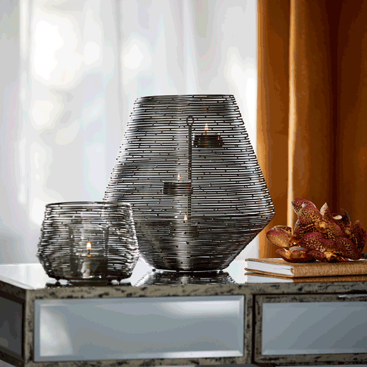 Spun Wire Votive Holder and Hurricane shown together with lit candles on a tab le with curtains in the background.