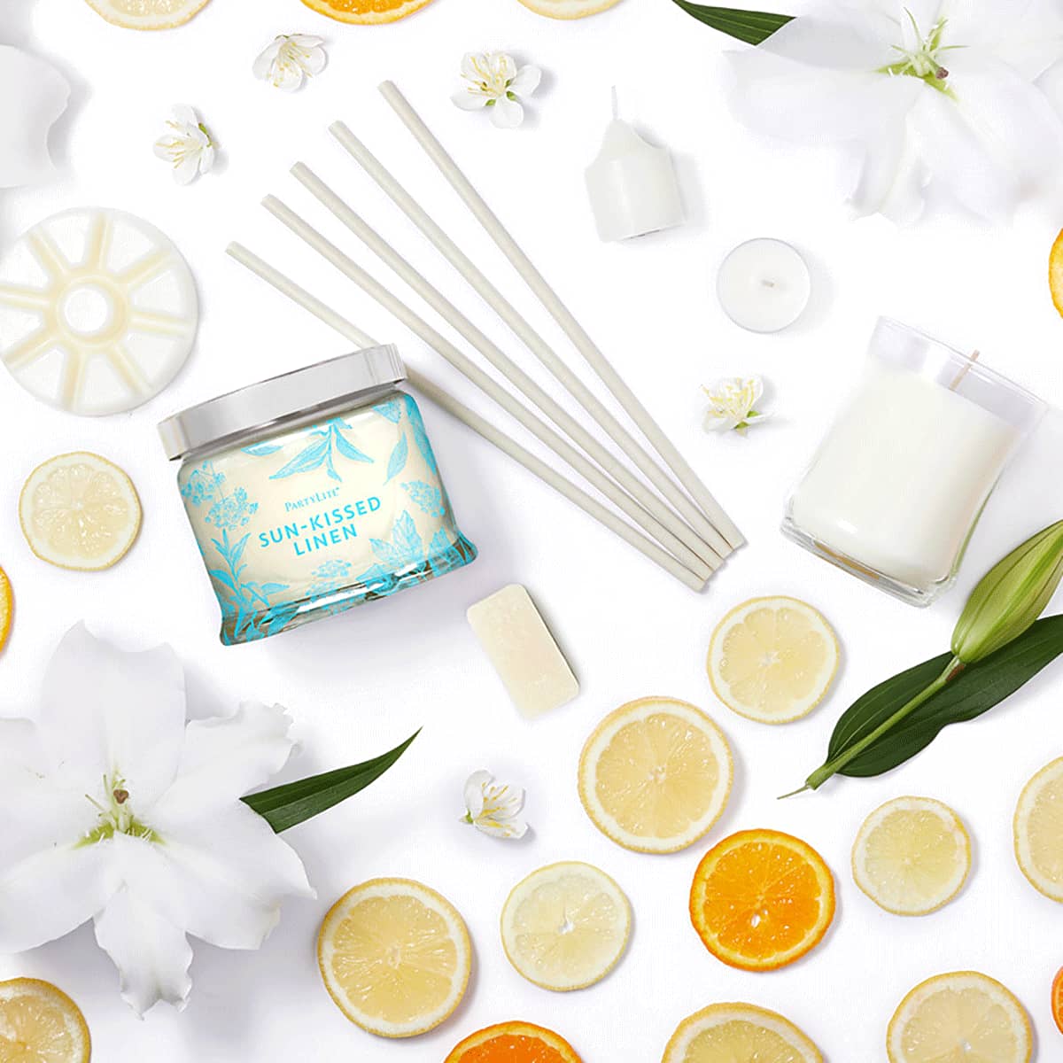Sun-Kissed Linen 3-wick jar candle, fragrance sticks, escential jar, votive, tealight and wax melts, surrounded by slices of oranges and lemons on a white background.