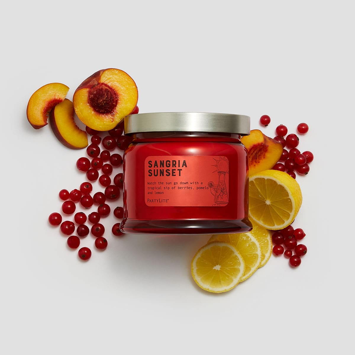 Sangria Sunset 3 Wick Jar Candle surrounded by pieces of fruit and berries against a white background.