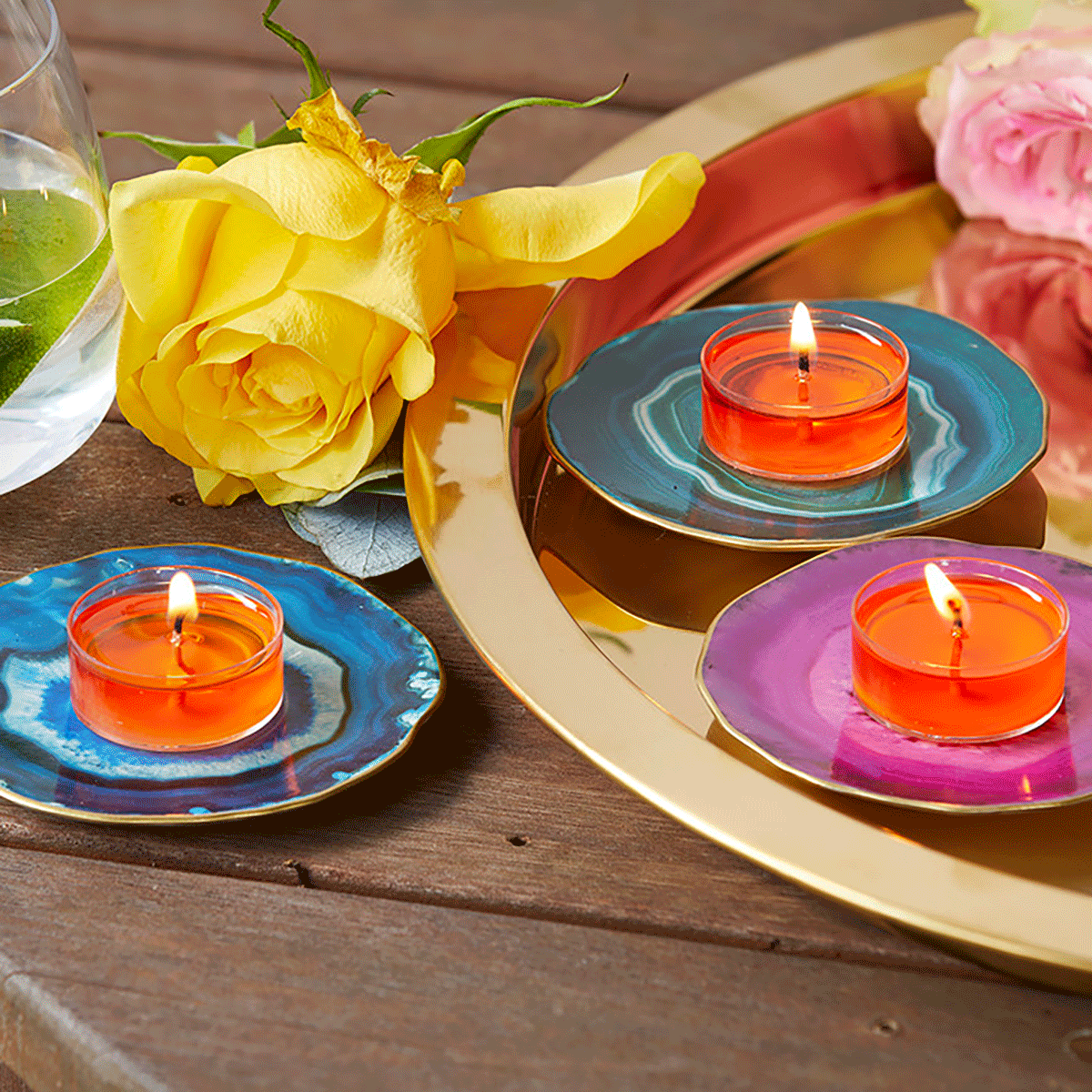 Faux Agate Tealight Holder Trio in blue, green and pink colors shown with lit tealighrts, with a yellow rose and a gold tray on a wooden table.