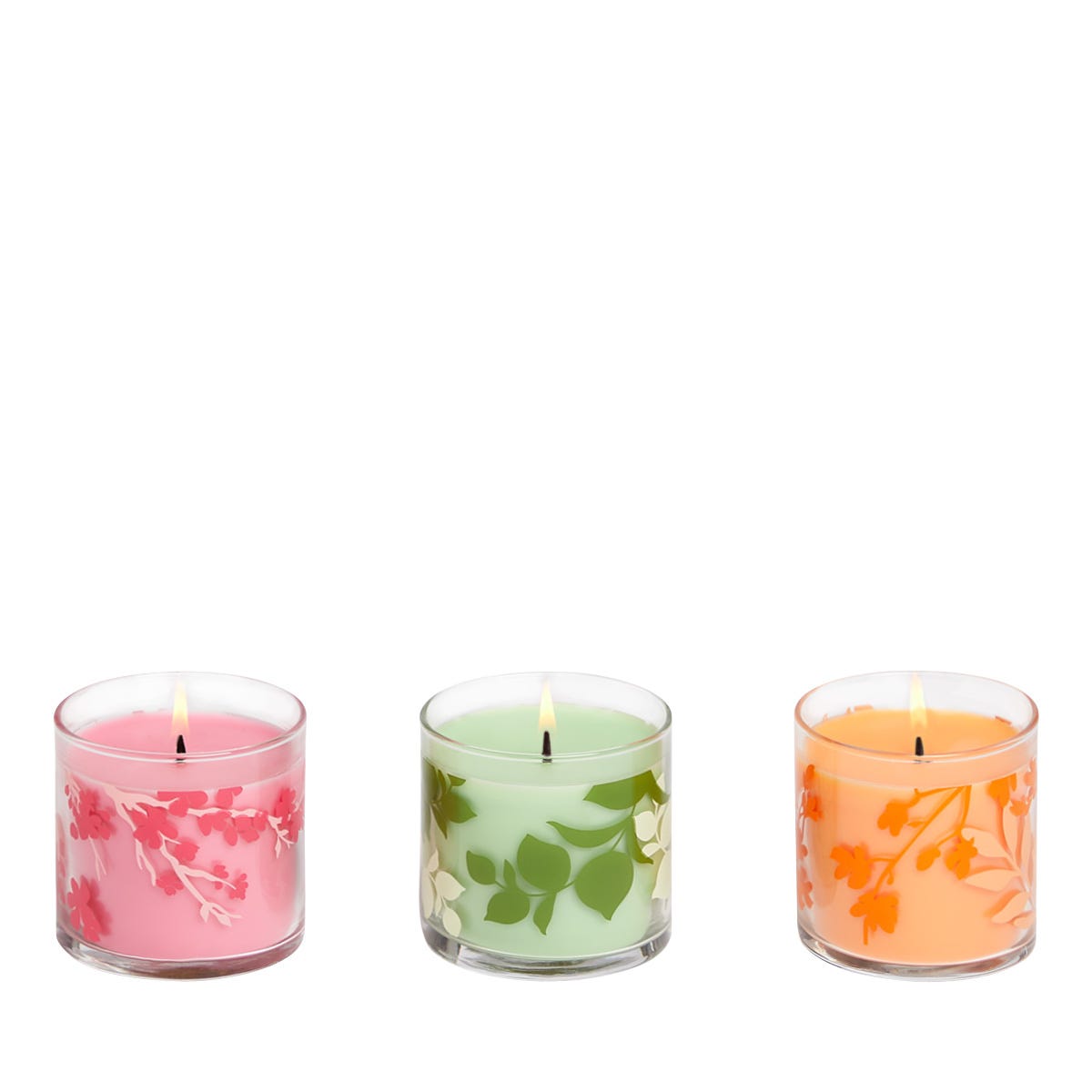 Three jar candles, each with a different fragrance, displayed side by side. From left to right, the candles are pink with a floral pattern, green with leaf patterns, and orange with what appears to be a floral pattern.