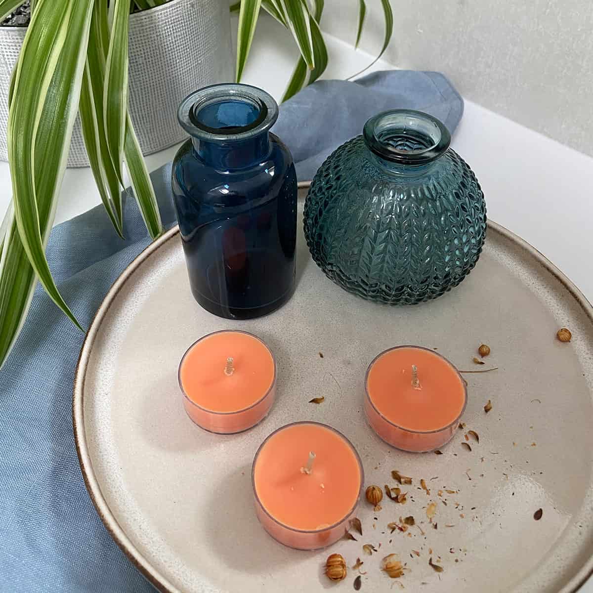 Fresh Home Bergamot Geranium Scented Orange Tealight Candles shown with colored vases on a light colored tray.