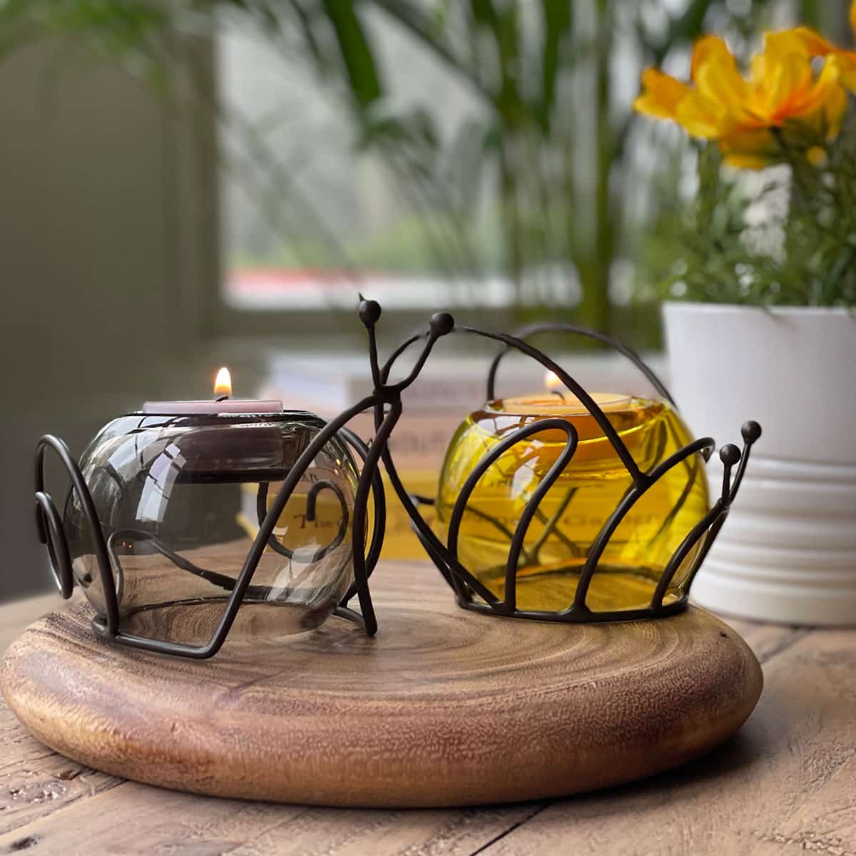 A dark metal tealight holder designed to resemble a bee, with a yellow glass globe for the body, shown with the snail tealight holden on a wooden surface.