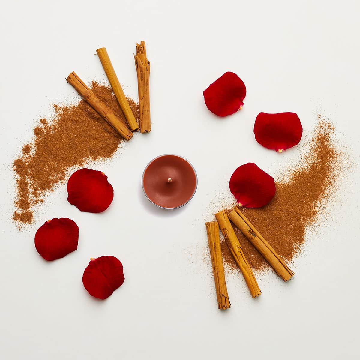 Cinnamon Sticks brown tealight, shown with grounded cinnamon and red flower leaves.
