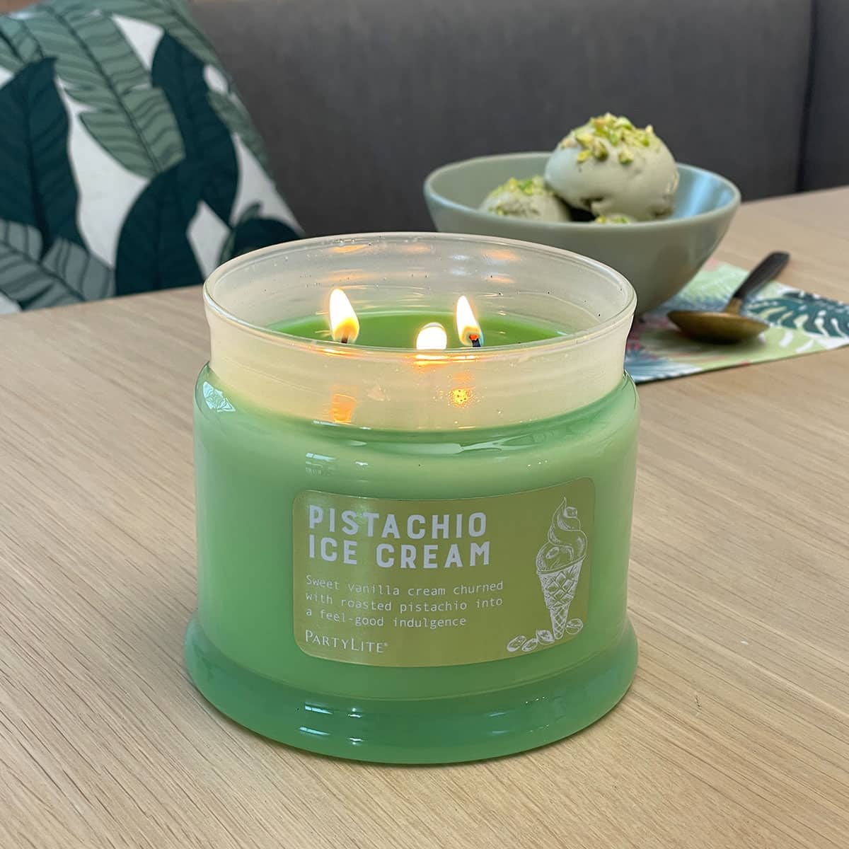 Pistachio Ice Cream 3-Wick Jar Candle lit on a wooden surface with a bowl of ice cream in the background.