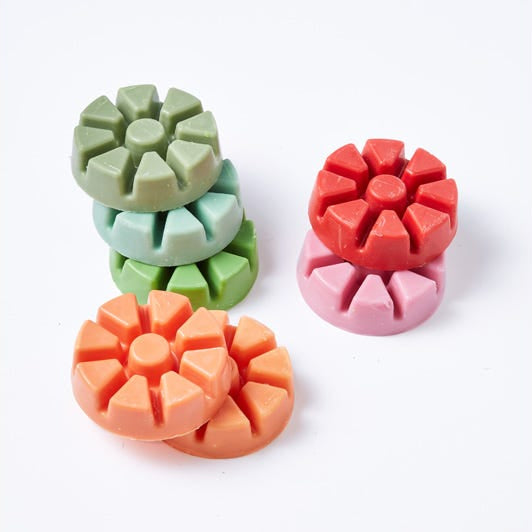 Various colored wax melts, in pink,green,orange against a white background.