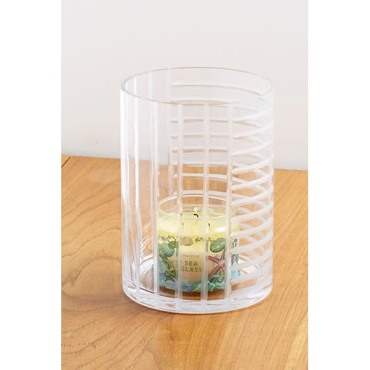 Linear Lines Glass Hurricane Candle Holder shown with a lit 3-wick jar on a wooden surface with a light background.