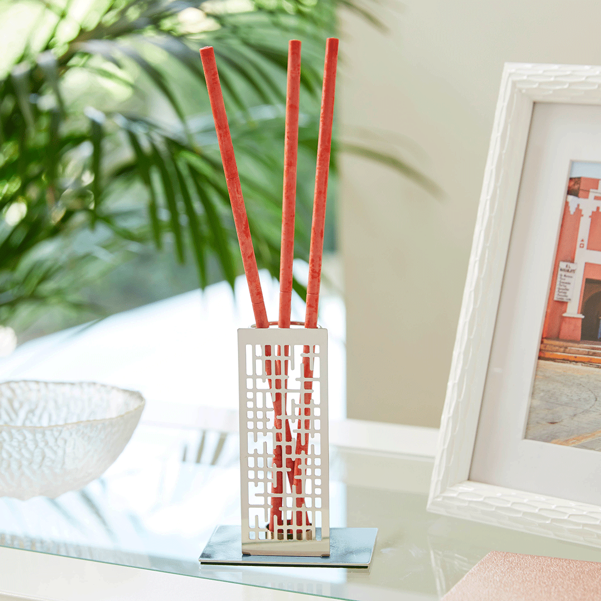Contempo silver metal smart scents holder shown with fragrance sticks ona shelf with a plant in the background.