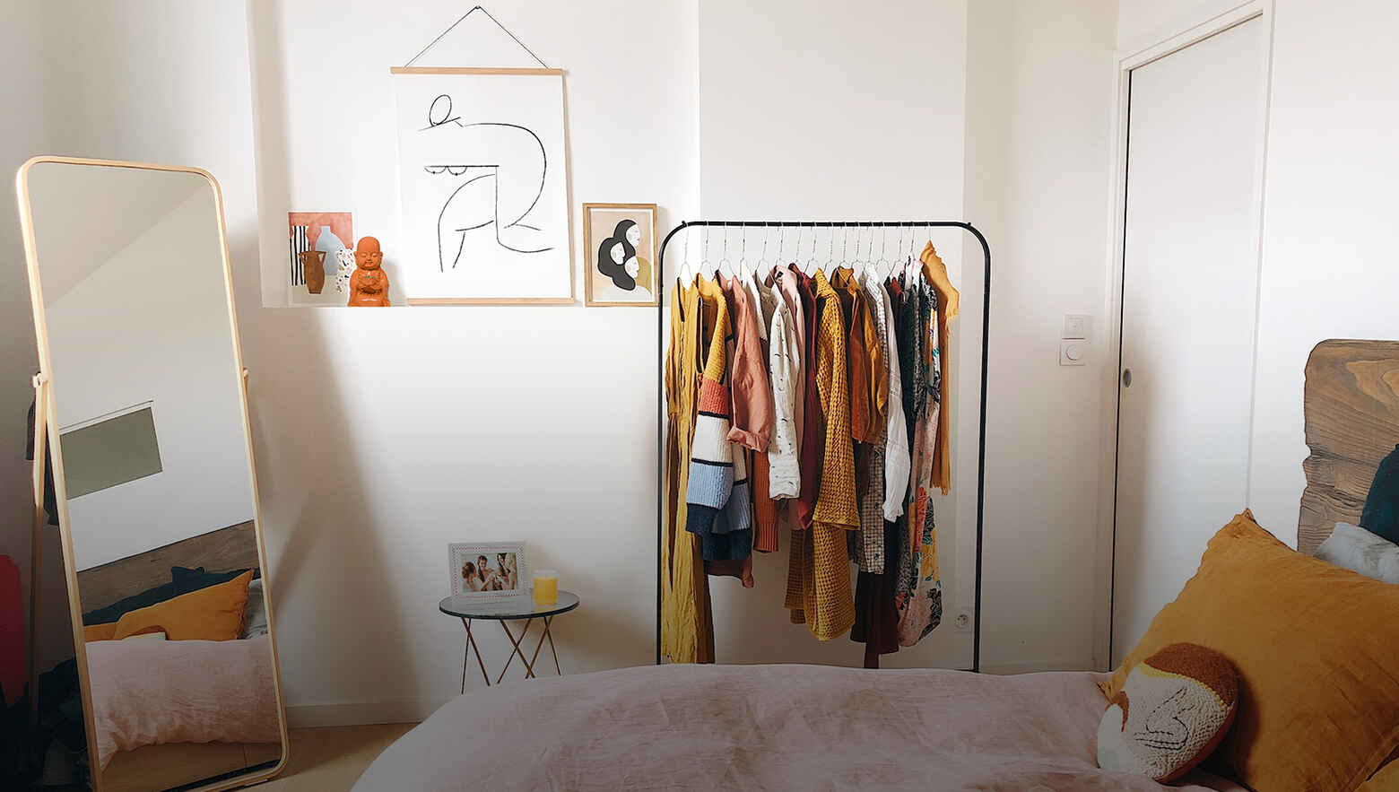 bedroom photo showing stand up mirror and a clothes rail with clothes and a bed.