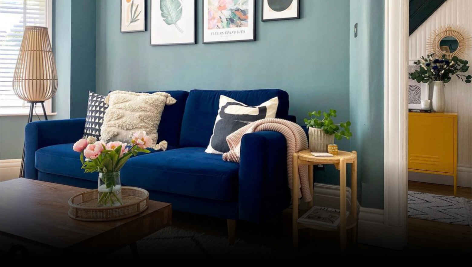 A cozy living room with a vibrant blue sofa adorned with patterned and textured pillows, framed by elegant wall art. A wooden coffee table displays fresh flowers, creating a warm, inviting atmosphere.