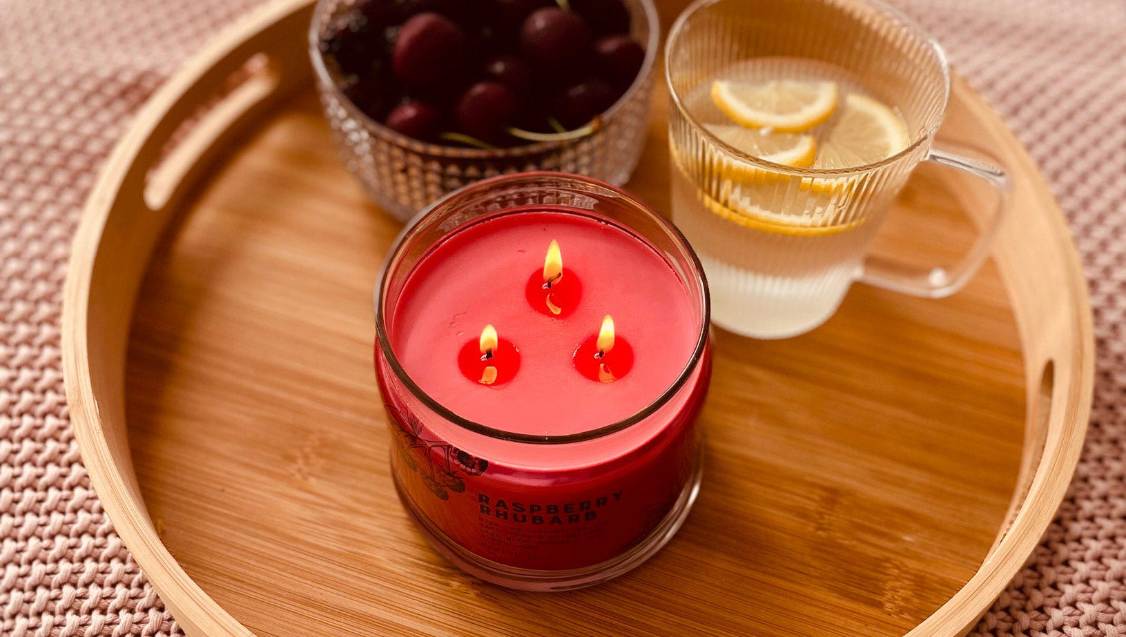 3-wick jar candle lit on a wooden round tray with a glass of lemon water.