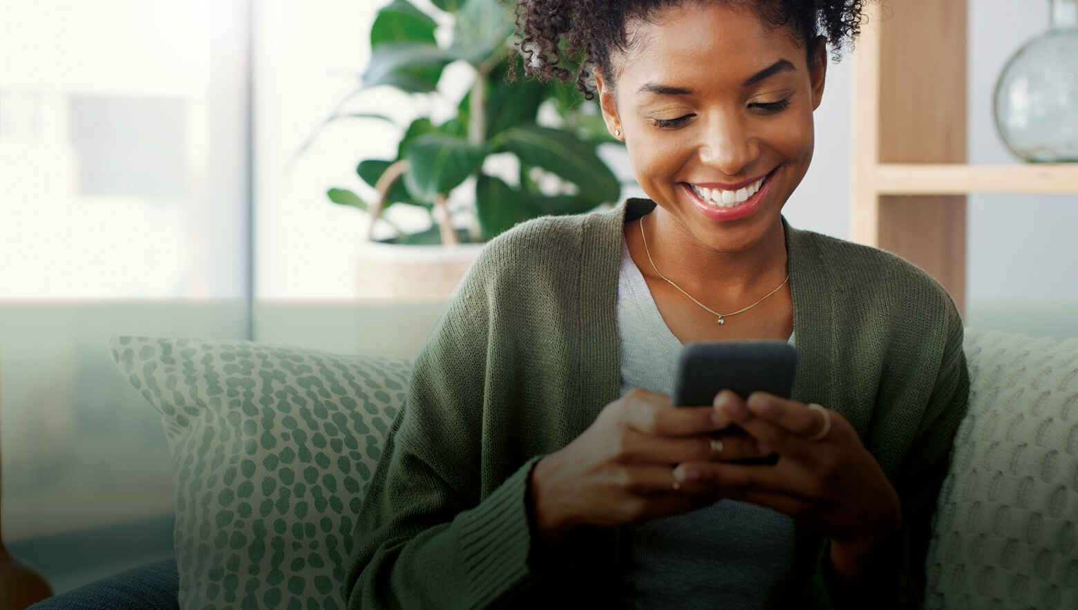 A lady smiling holding her phone in a living room setting.