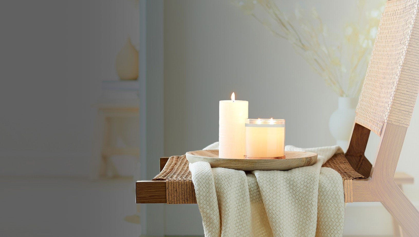 Pillar candle and a jar candle shown lit on a tray on a chair.